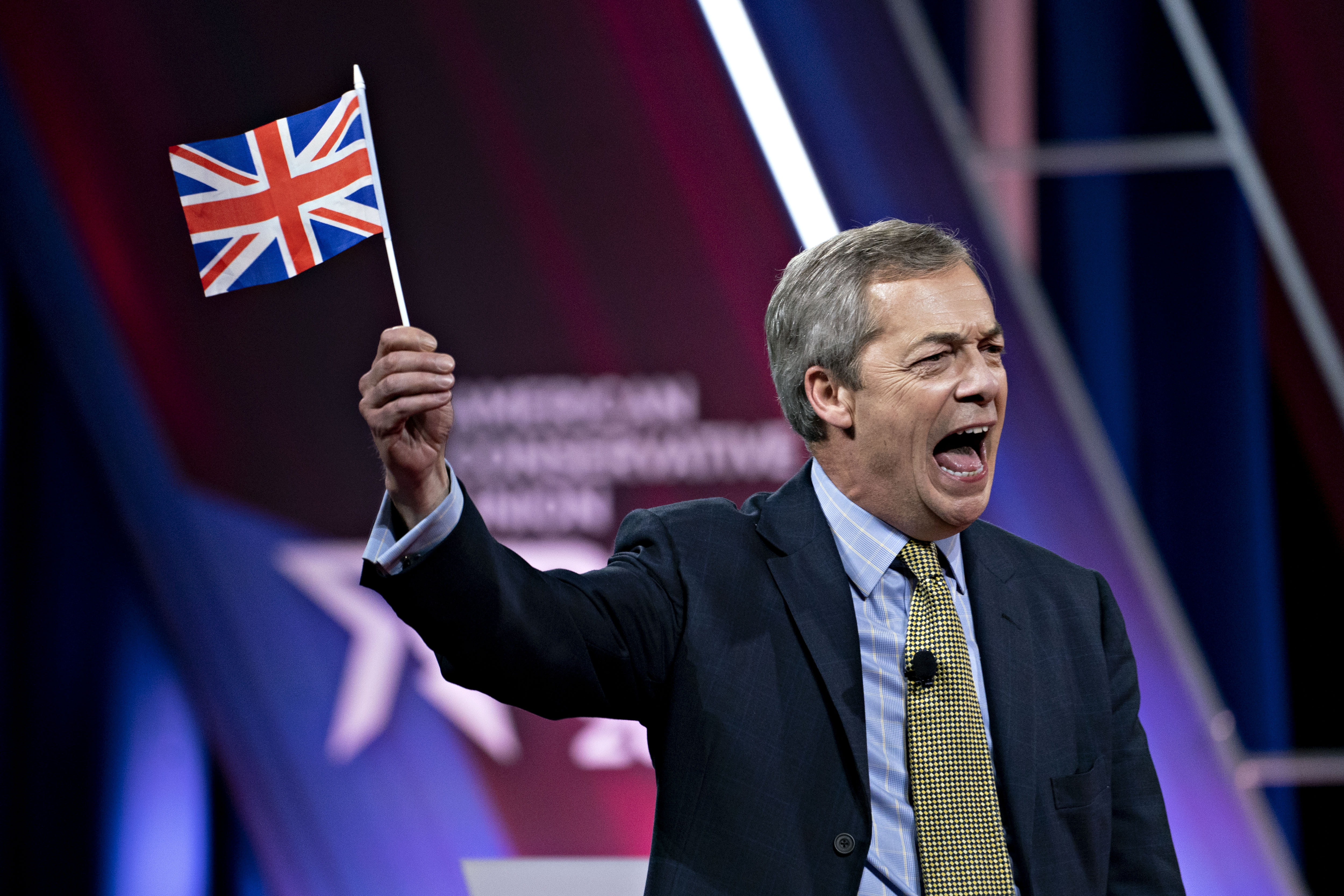 Nigel Farage, leader of the Brexit Party, holds a British Union flag and shouts while speaking at CPAC.