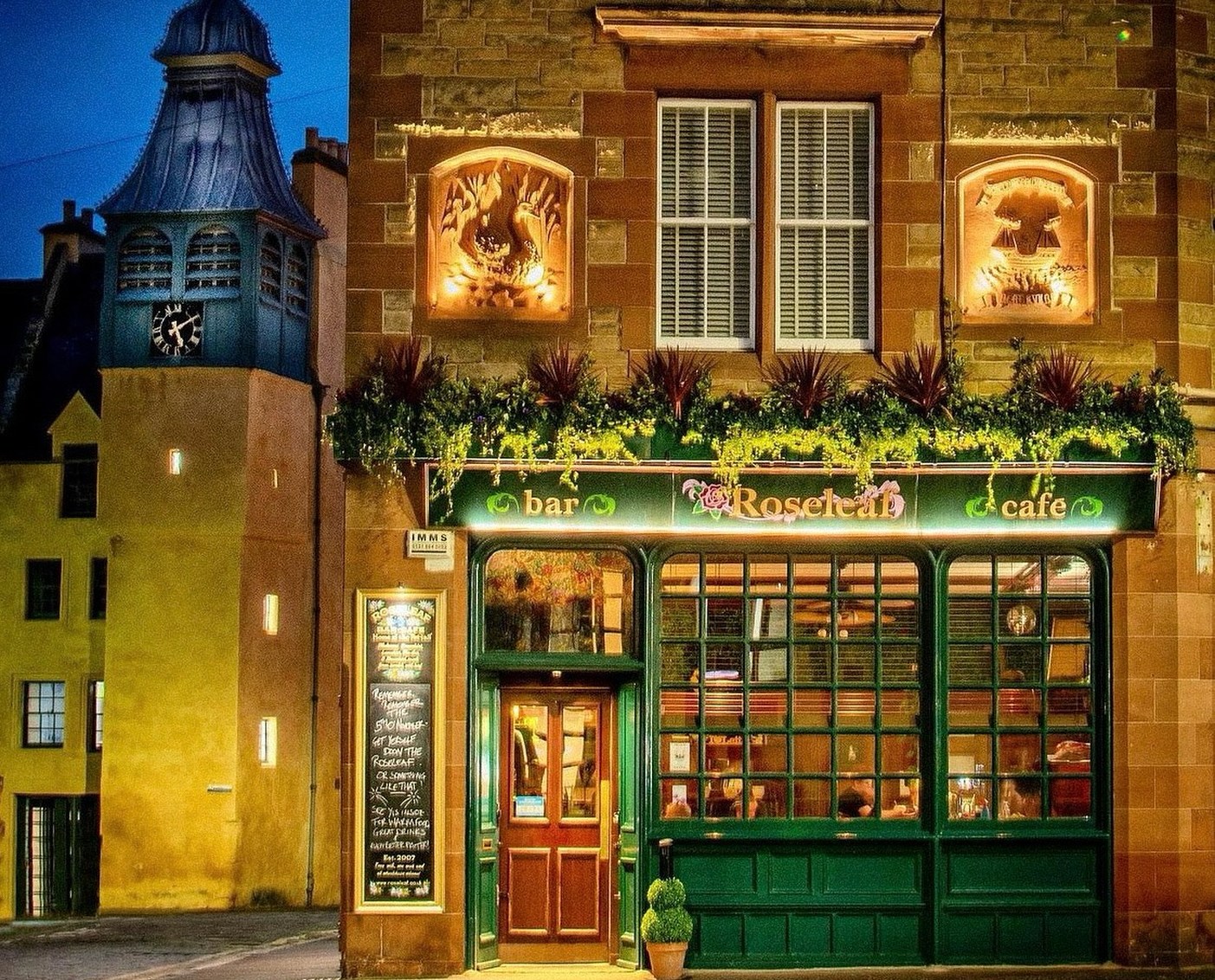 The Roseleaf Bar and Cafe in Edinburgh at night, with a clock tower visible in the background.