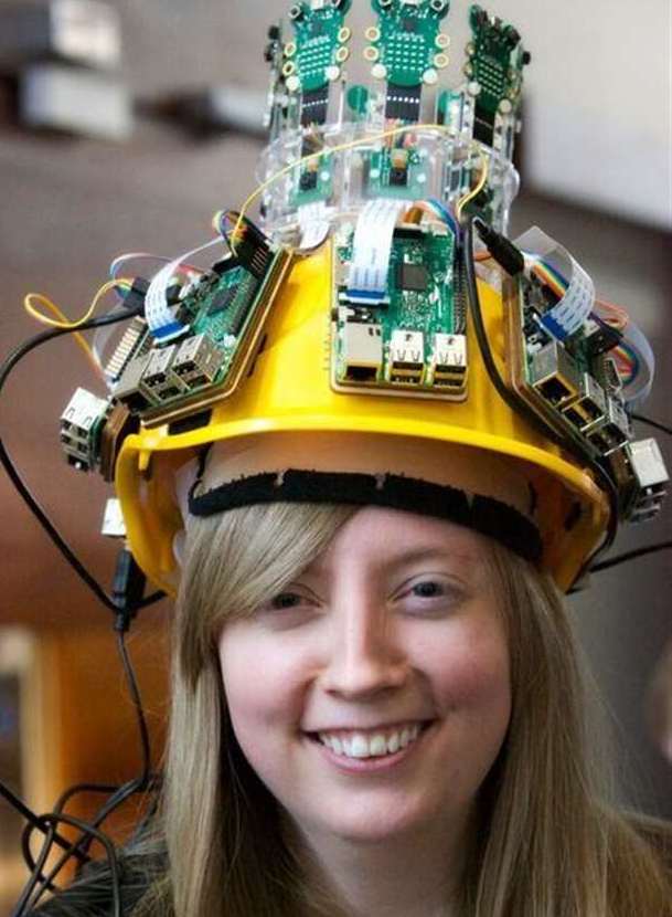Carrie Anne Philbin wearing a yellow hard hat adorned with Raspberry Pi boards, microcontrollers, and wiring.