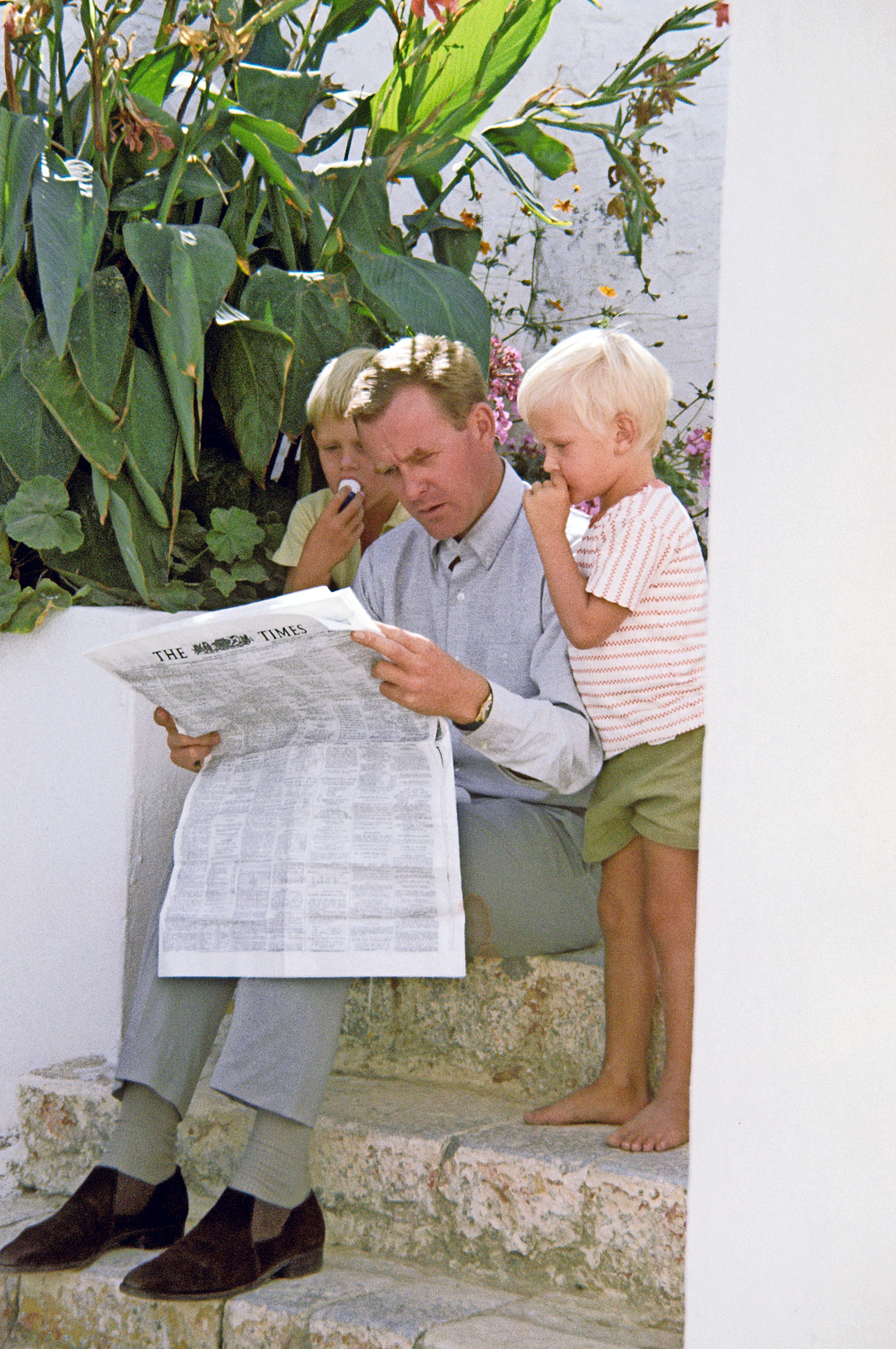 John le Carré reading The Times on steps with his two sons in Spetsai, Greece.