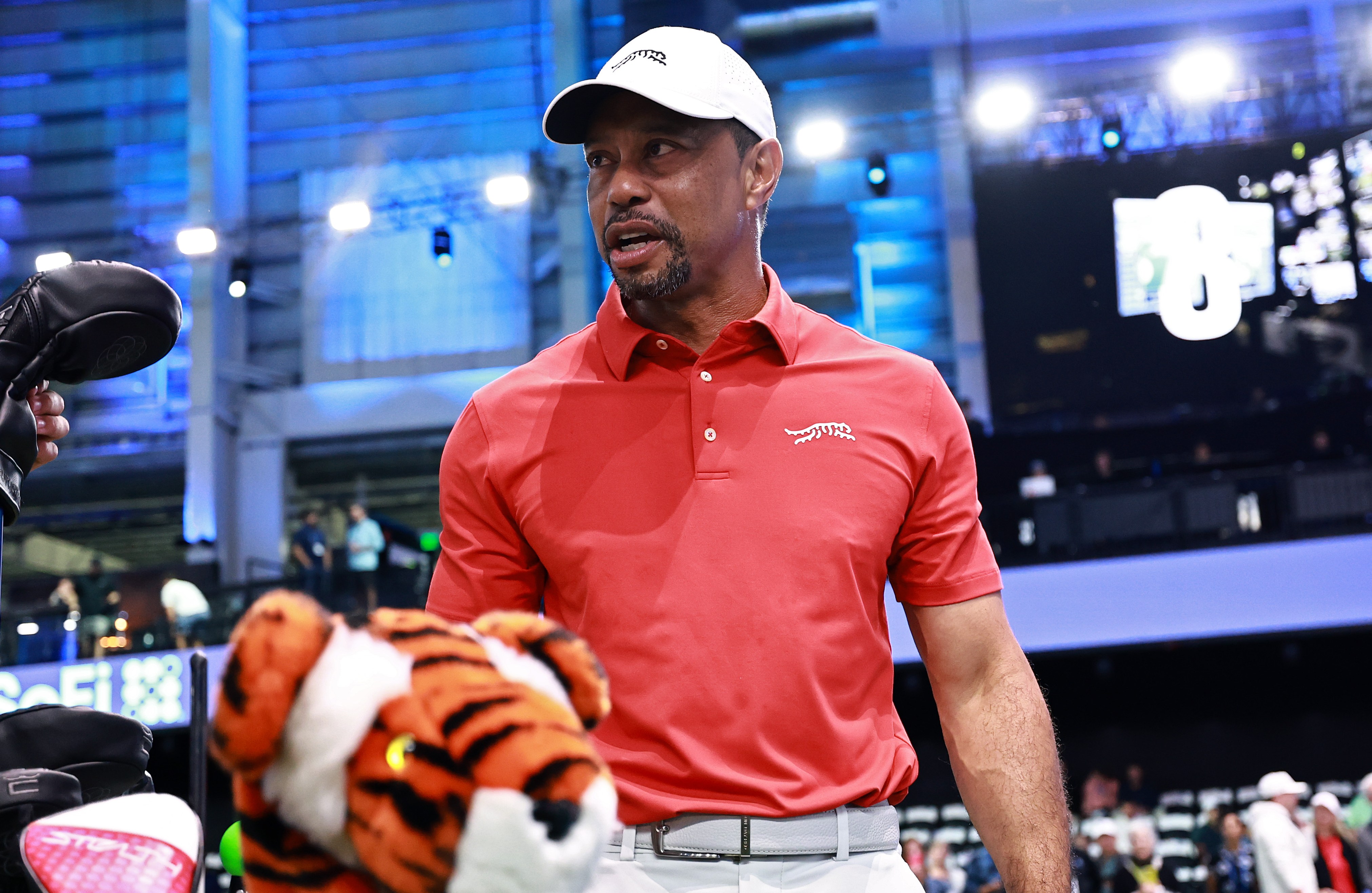 Tiger Woods warming up before a TGL match, standing next to a golf bag with a tiger head cover.