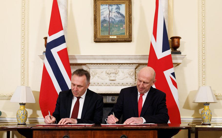 Two men sit next to each other and sign an agreement.