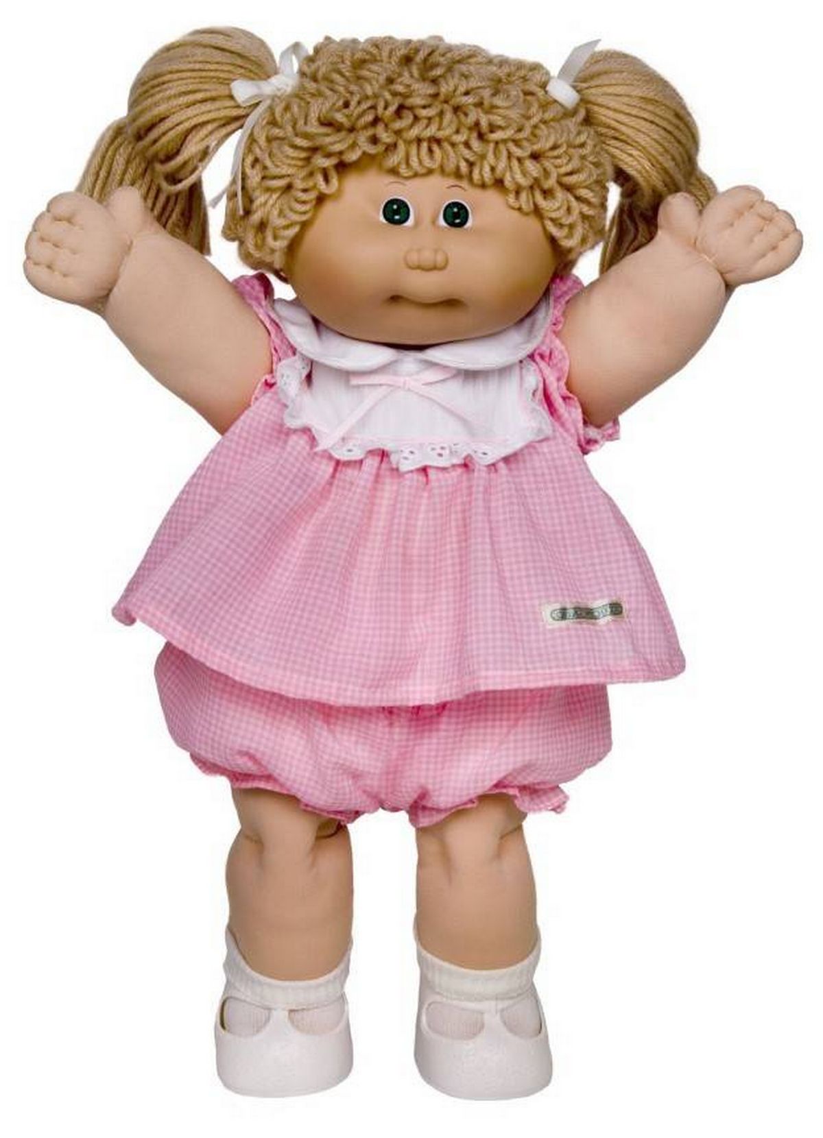 A close-up of a vinyl doll with brown curly hair, dressed in a pink dress with ruffled details, standing with both arms raised. The doll has a neutral facial expression.