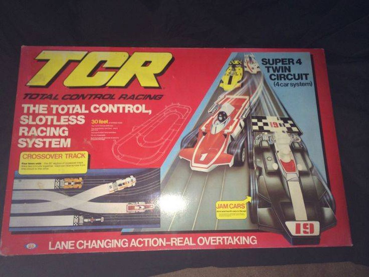 A box for the Total Control Racing System, prominently displaying the TCR logo in bold, capitalized letters, set against a dynamic background featuring an illustration of a racing vehicle in motion, with additional text highlighting the product's features.