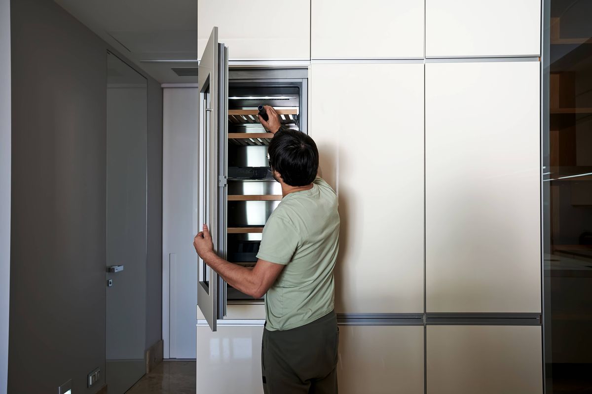 A middle-aged man picks out wine from a wine cabinet.