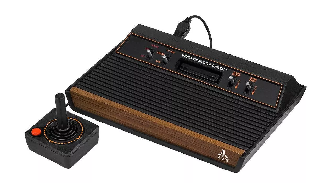 An image displays a vintage black and brown gaming console with a joystick placed beside it on a white background.
