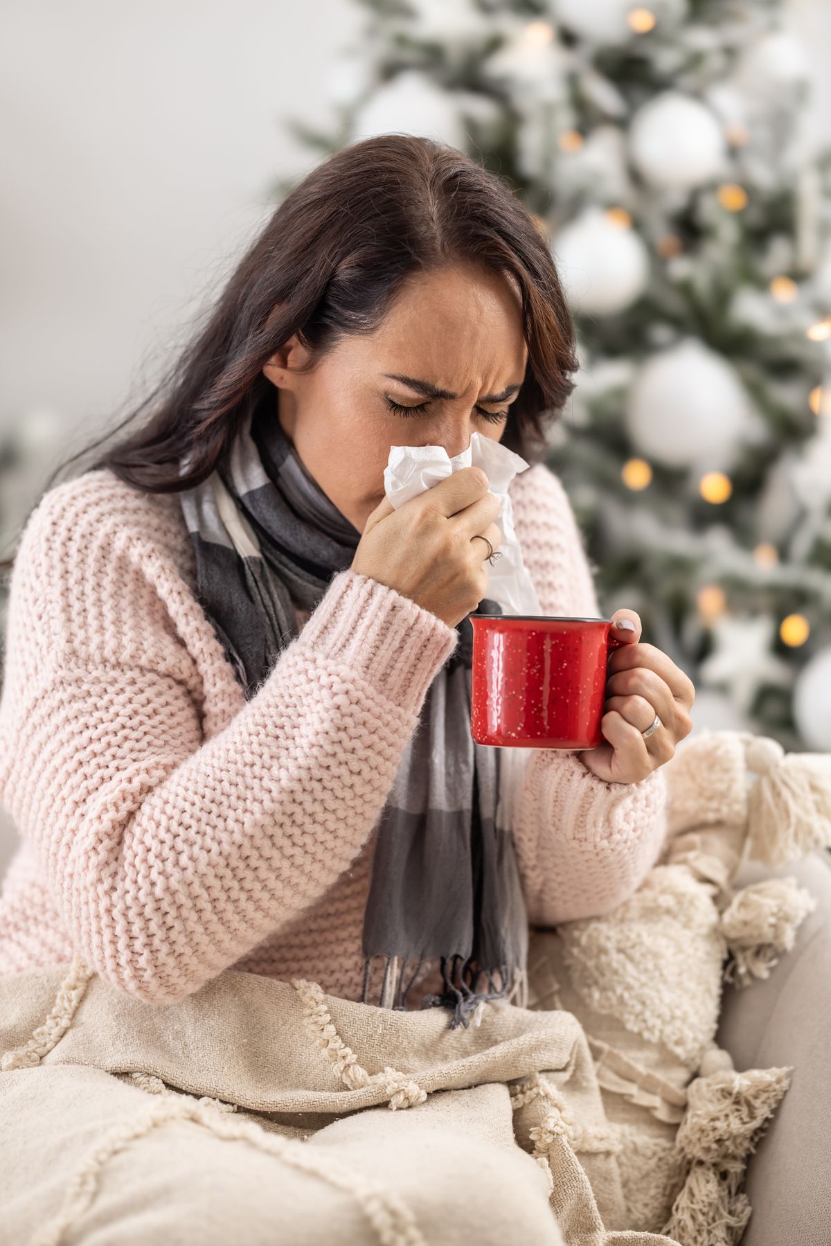 Woman sneezing into a tissue in front of a Christmas tree