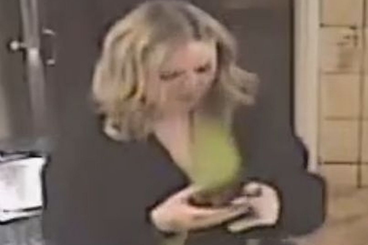CCTV image of a blonde woman who is wearing a black and green top, with a black skirt and tights