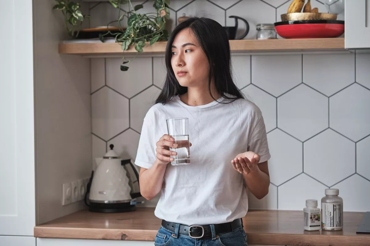 Sad depressed Asian woman holding pills and glass of water
