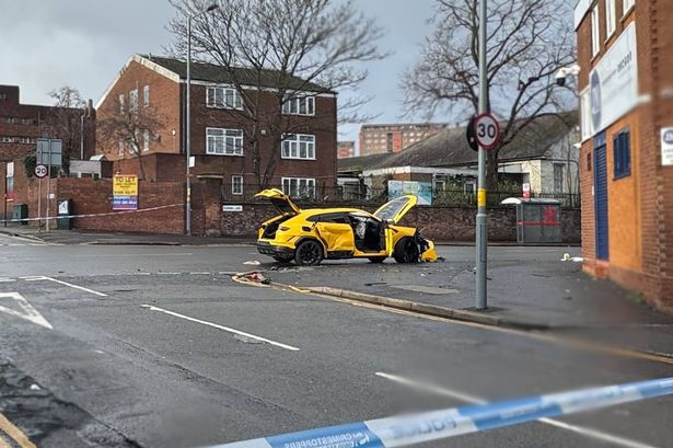 A yellow Lamborghini Urus sits damaged in the middle of a road after a crash  