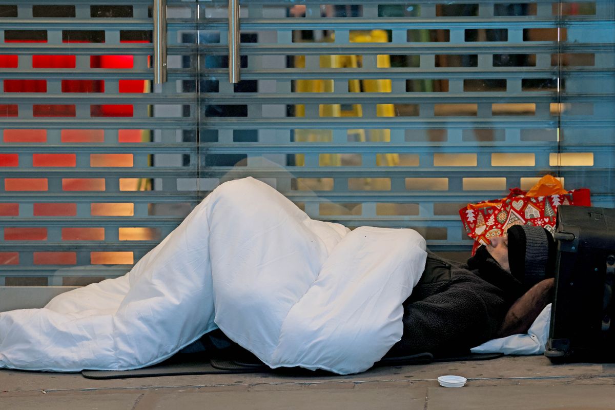 A homeless man sleeps on the doorway of a closed shop in the city centre