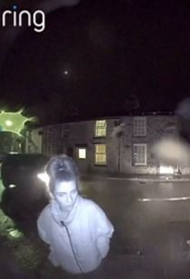 A woman with dark hair in a high bun, hands in coat pocket