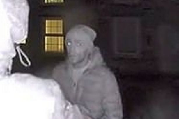 A man in a coat and hat talking to a hooded figure