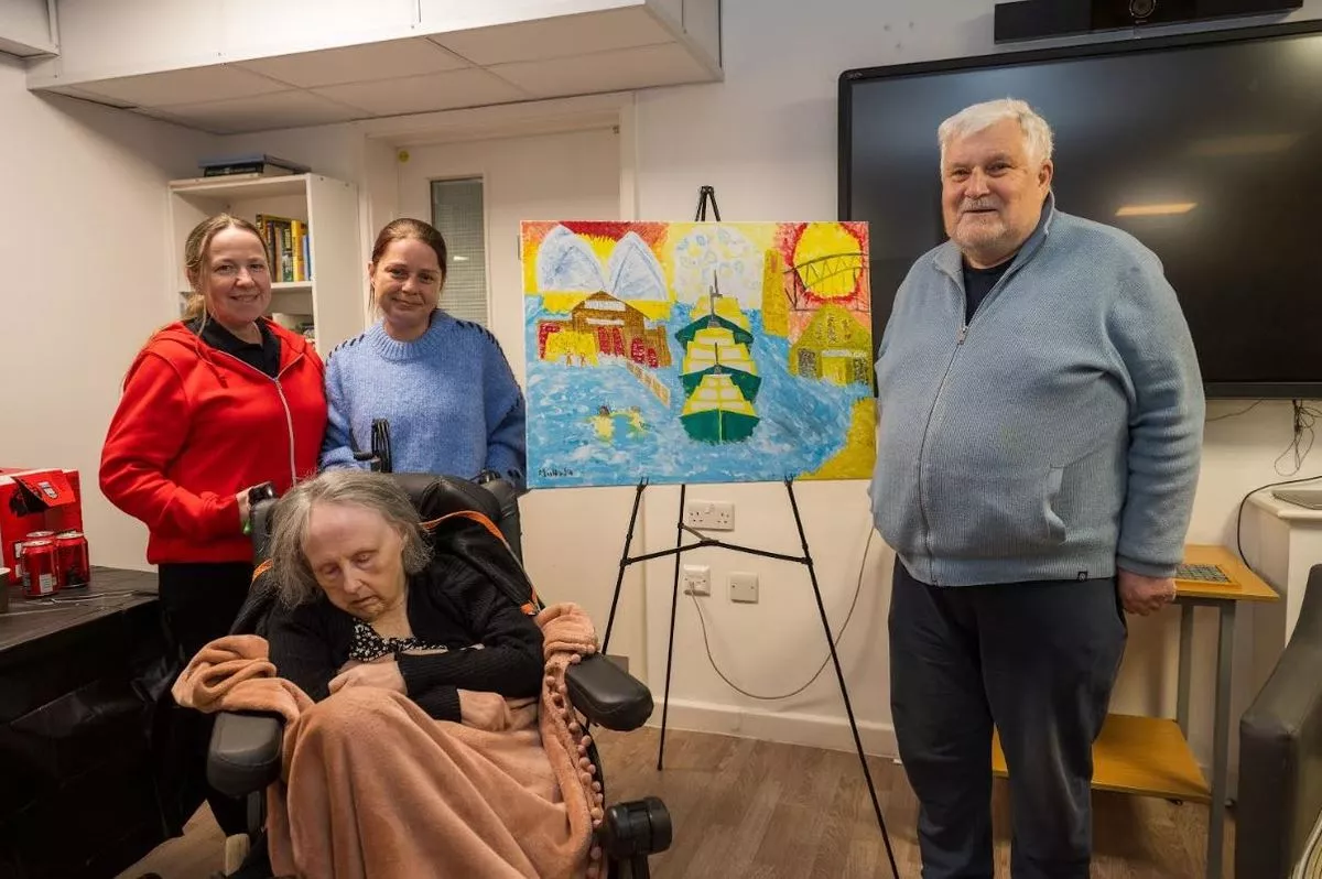 A woman in a wheelchair and an older gentleman smiling next to a colourful easel