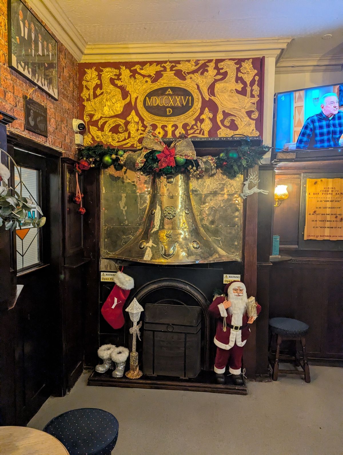 A large brass fireplace above a wood-burning stove. A figure of Santa and a stocking flank the stove. A crest above bears the Roman date: "MDCCXXVI AD" (1726 AD)