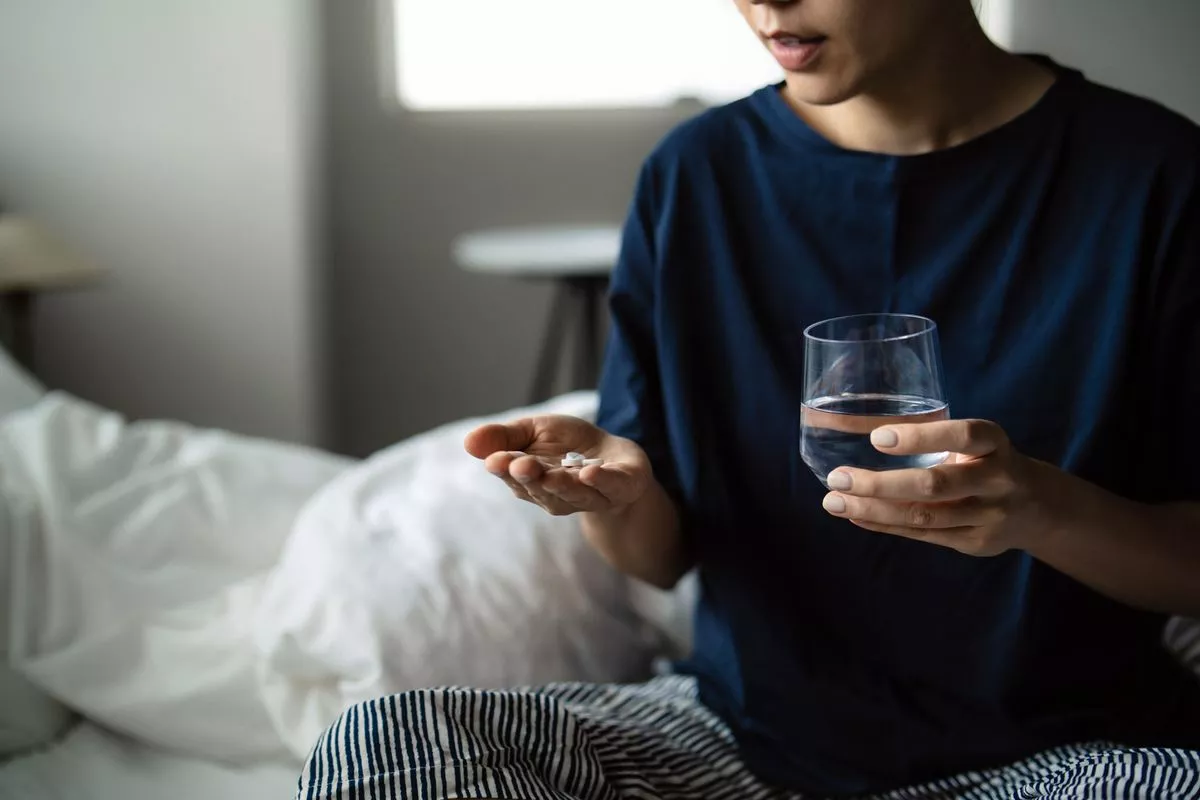 Cropped shot of young Asian woman taking medicines in hand with a glass of water at home. Feeling sick. Medicine, healthcare, supplements and wellbeing concepts