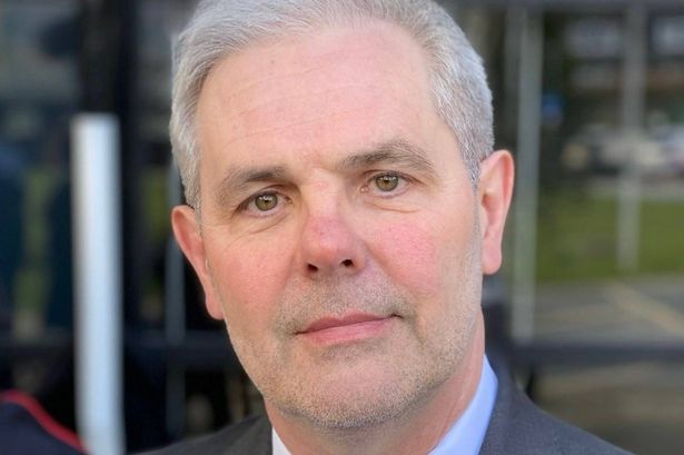 A man in early fifties, white hair, wearing a suit