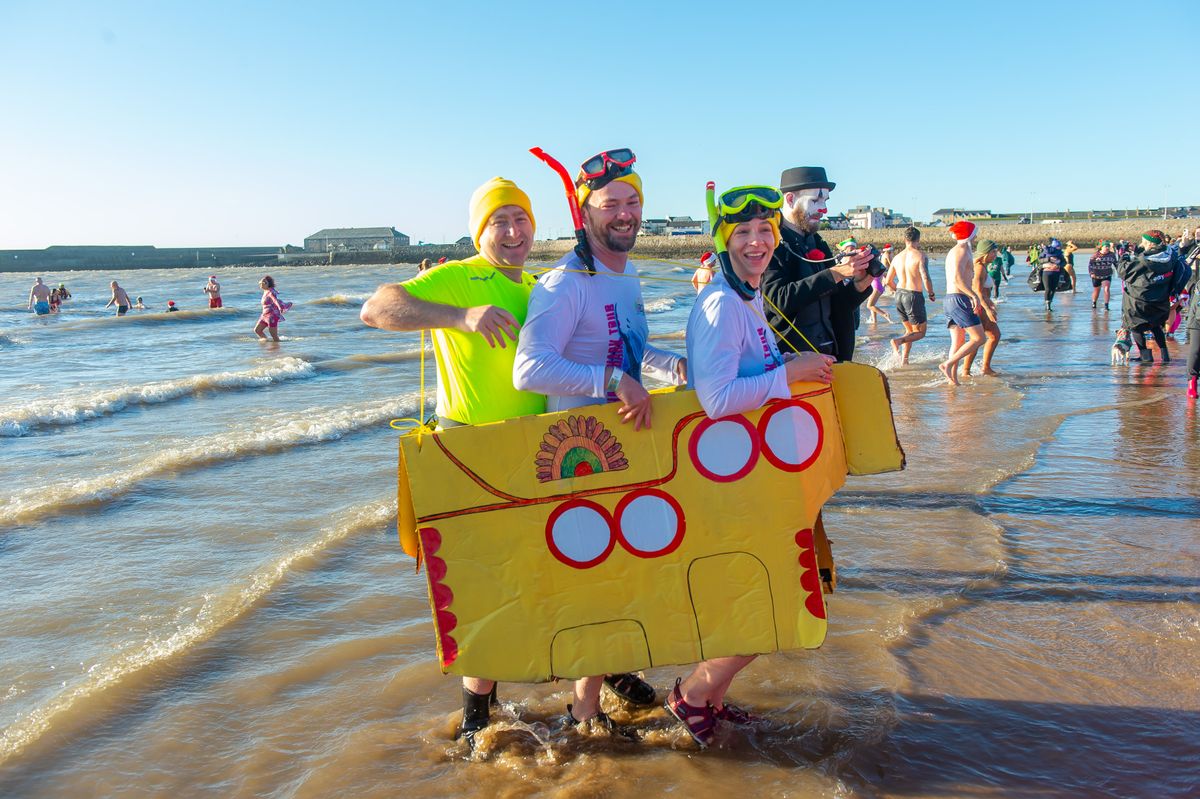 The image shows swimmers in fancy dress on the beach
