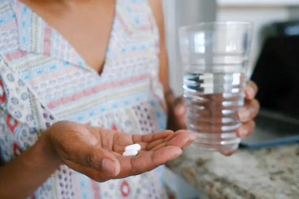 Close-up of unrecognizable black woman in kitchen taking break from working on laptop to take medication
