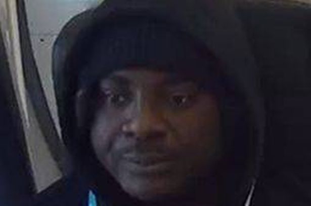 Black man in his 40s wearing a black hoodie sat on a train