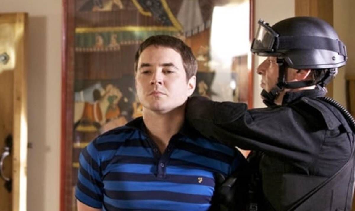 A man in a blue striped shirt is arrested by the police