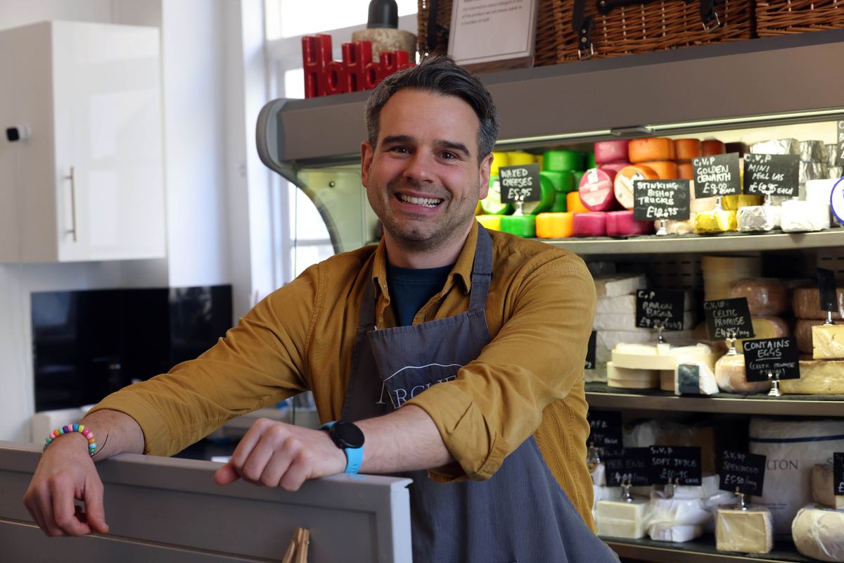 A man with dark hair, smiling behind a till