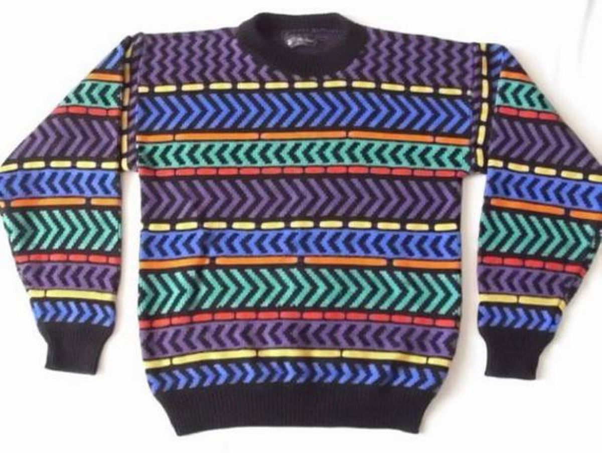 A vibrant, multicolored sweater featuring a pattern of chevrons is displayed against a plain background. The sweater is composed of various shades of blue, green, red, and yellow, creating a dynamic and visually striking design. The sleeves and hem of the garment are finished with black cuffs, adding a contrast to the overall colorful pattern.