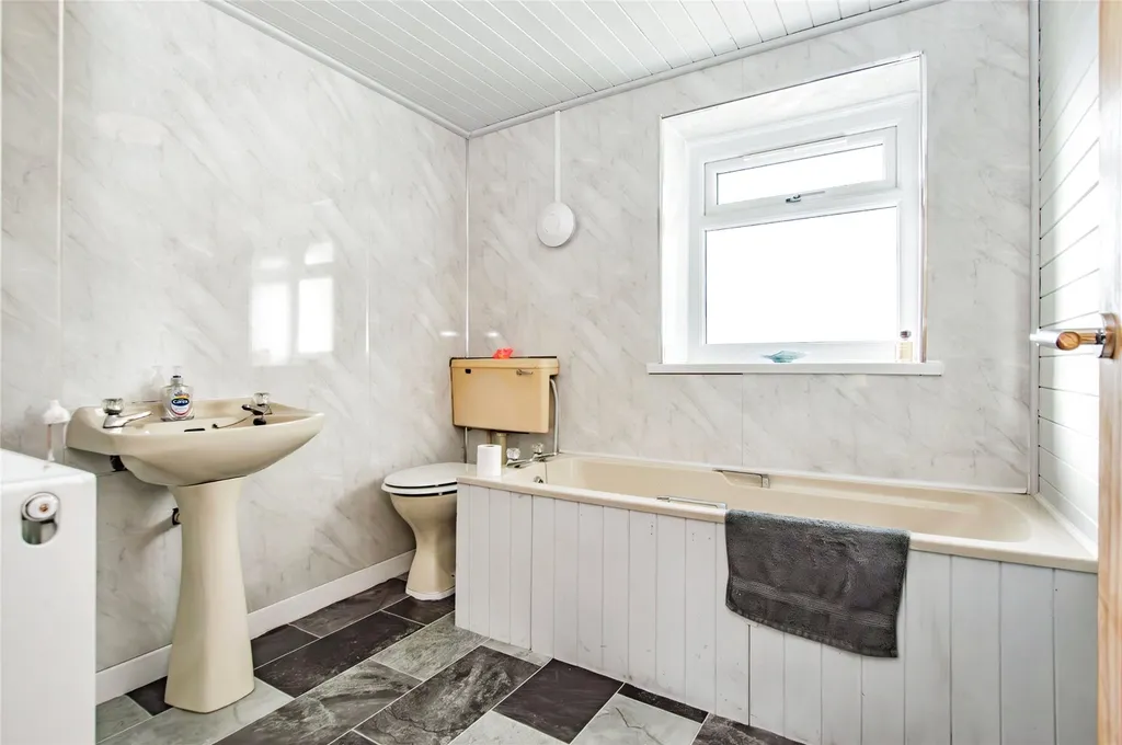 Bathroom with beige fixtures, marble-effect walls, frosted window and grey tiled floor.