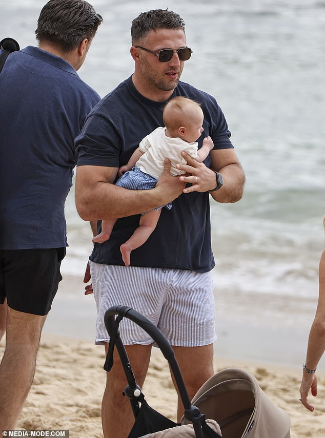 Sam was every inch the doting father as he cradled the couple¿s three-month-old son Mack close to his chest while standing at the water's edge, carefully shielding the newborn from the gentle waves