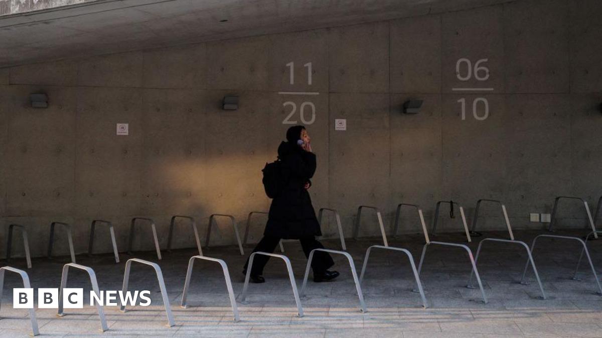 A young woman wearing a full black outfit talking on her phone as she walks