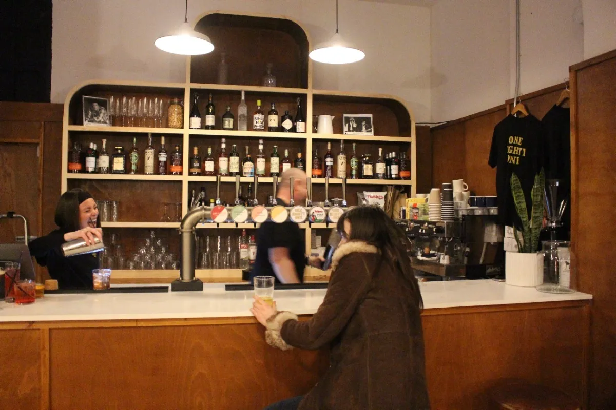 Woman in a brown coat with fur cuffs sits at bar and orders a drink
