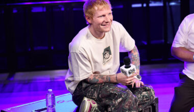 Ed Sheeran performing on stage with a guitar, passionately singing to a large audience at a music event.