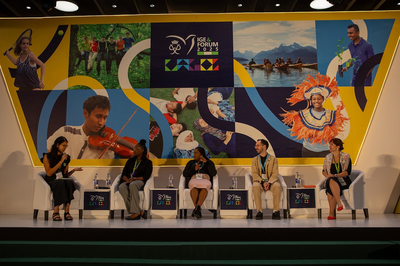 Four people sit in chairs on a stage.