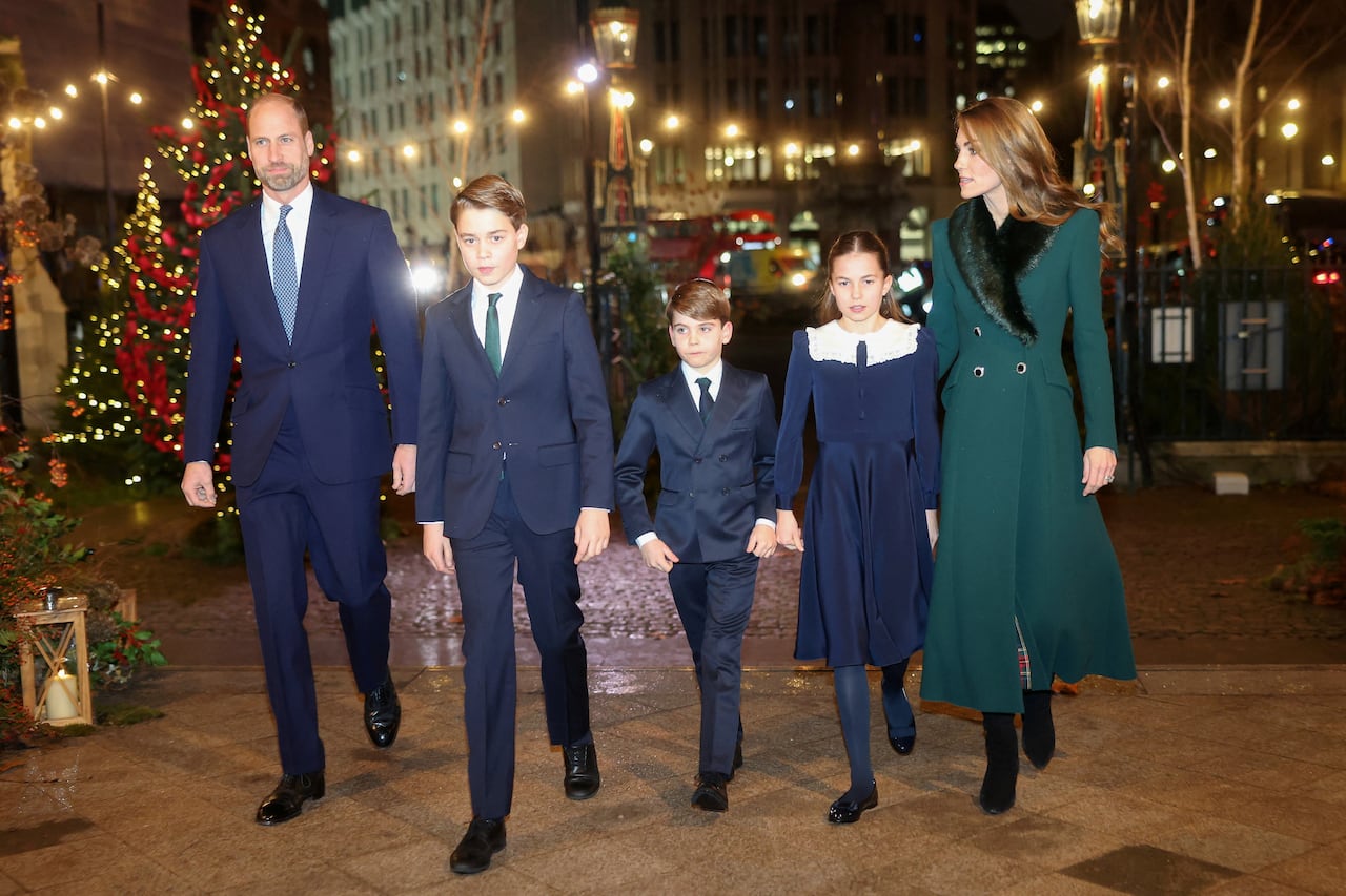 Two adults walk with three children between them and Christmas trees in the background.