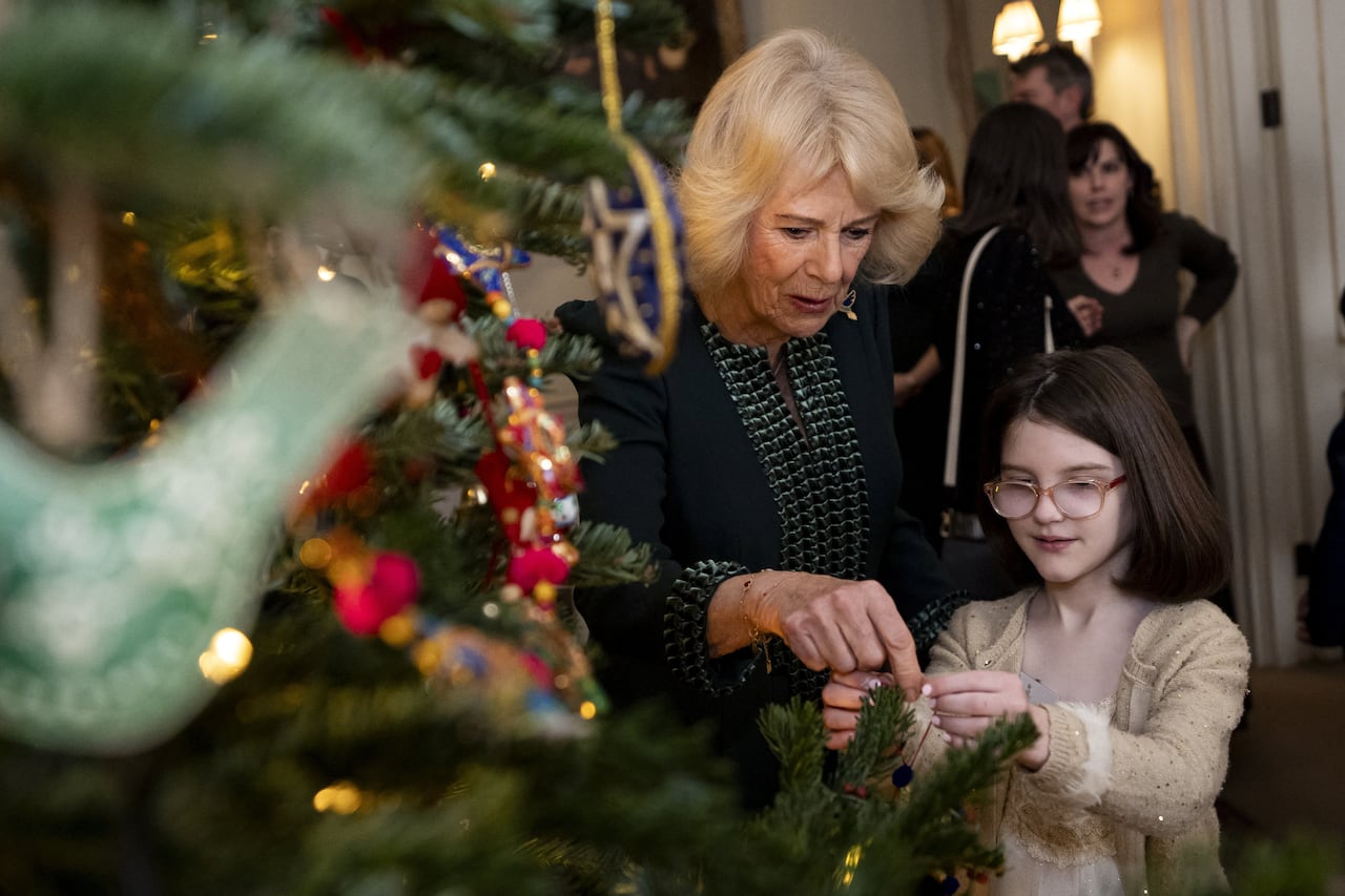 An adult helps a child hang an ornament on a Christmas tree.