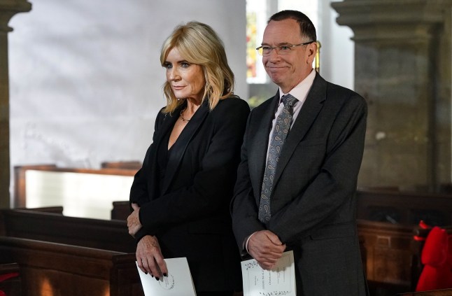 Cindy Beale standing with Ian in church in EastEnders, both wearing black suits.