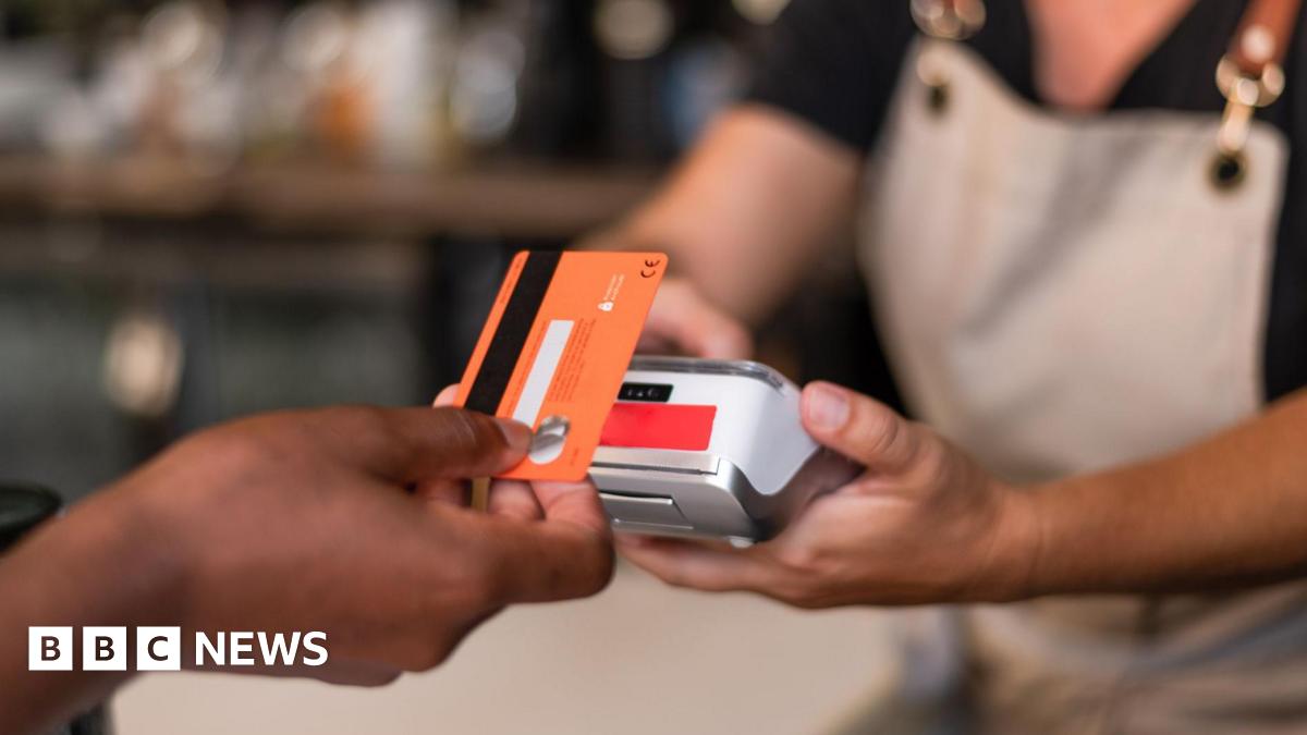 Contactless card payment being made with a card held in a hand and a terminal being held by someone in an apron.
