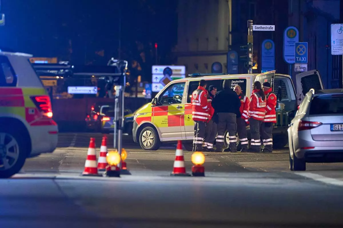 Emergency services from the German Red Cross (DRK) stand next to an emergency vehicle, at the site where a car is said to have driven into a bus stop and several people were injured, according to the police, in Giessen, Germany, Monday Dec. 22, 2025. (Sascha Ditscher/dpa via AP)