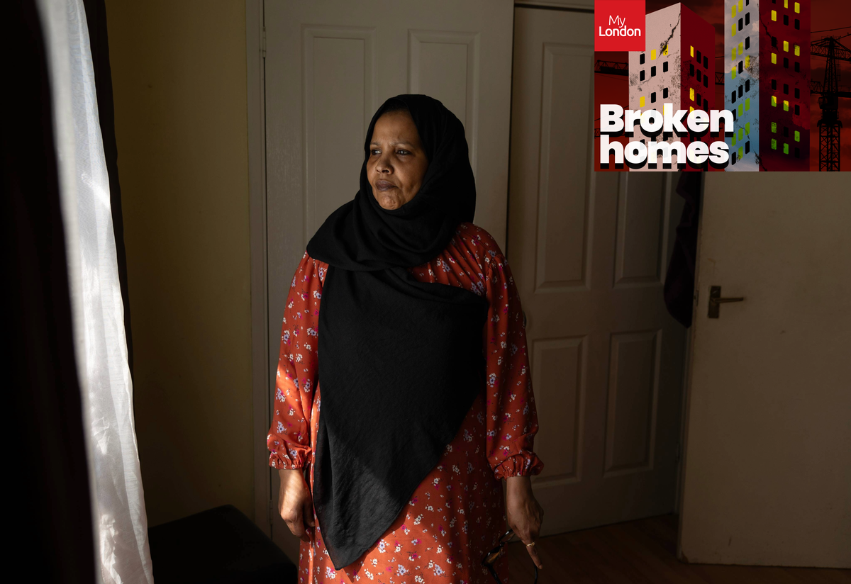 A woman in a traditional headscarf looks out of a window at her home