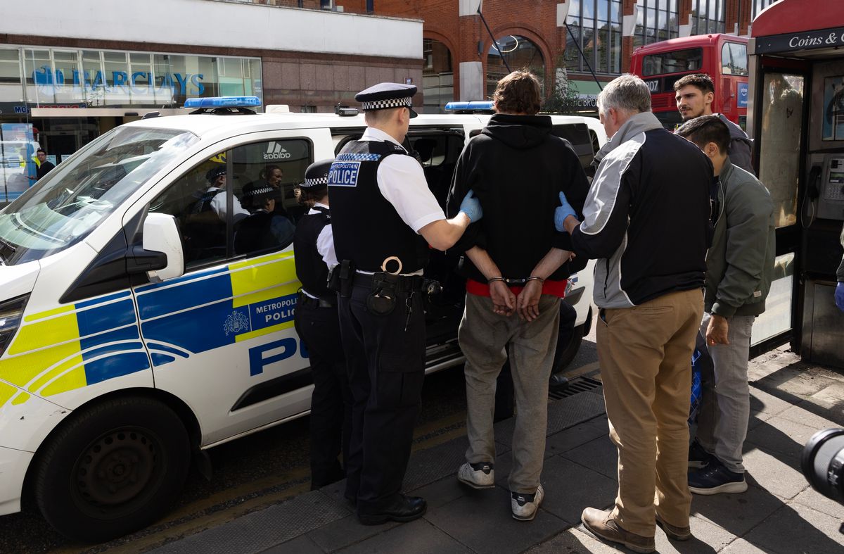 Police leading a man handcuffed into the side door of a police van in Ealing