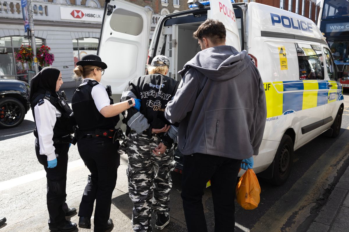 Police leading a handcuffed man into the back of a police van during an operation in Ealing 