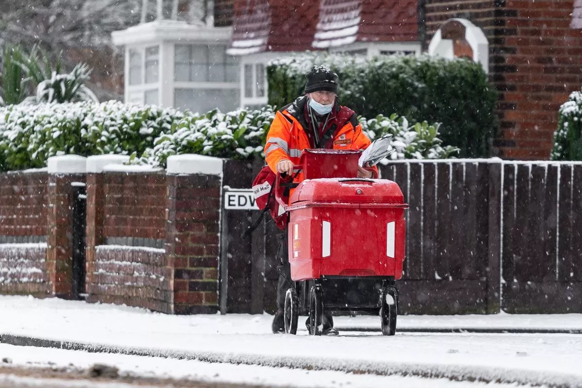 Mansfield Nottingham UK January 12th 2021 Royal Mail British post man in deep cold snow falling on road and icy frozen pavement delivering letters with trolley red uniform during severe weather
