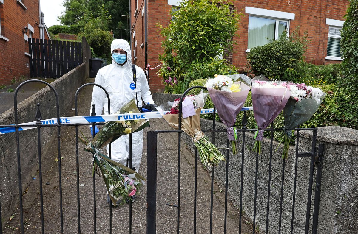Flowers at Marie Green's house on Wednesday with forensic officer in white overalls behind gate 