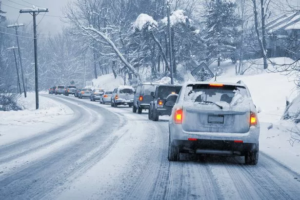 A line of cars slowly driving on a snowy, icy road