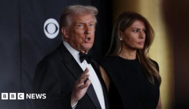President Donald Trump and first lady Melania Trump pose on the red carpet for the 2025 Kennedy Center Honors. Trump, in a tuxedo, tooks towards the camera as he gesture while speaking to reporters