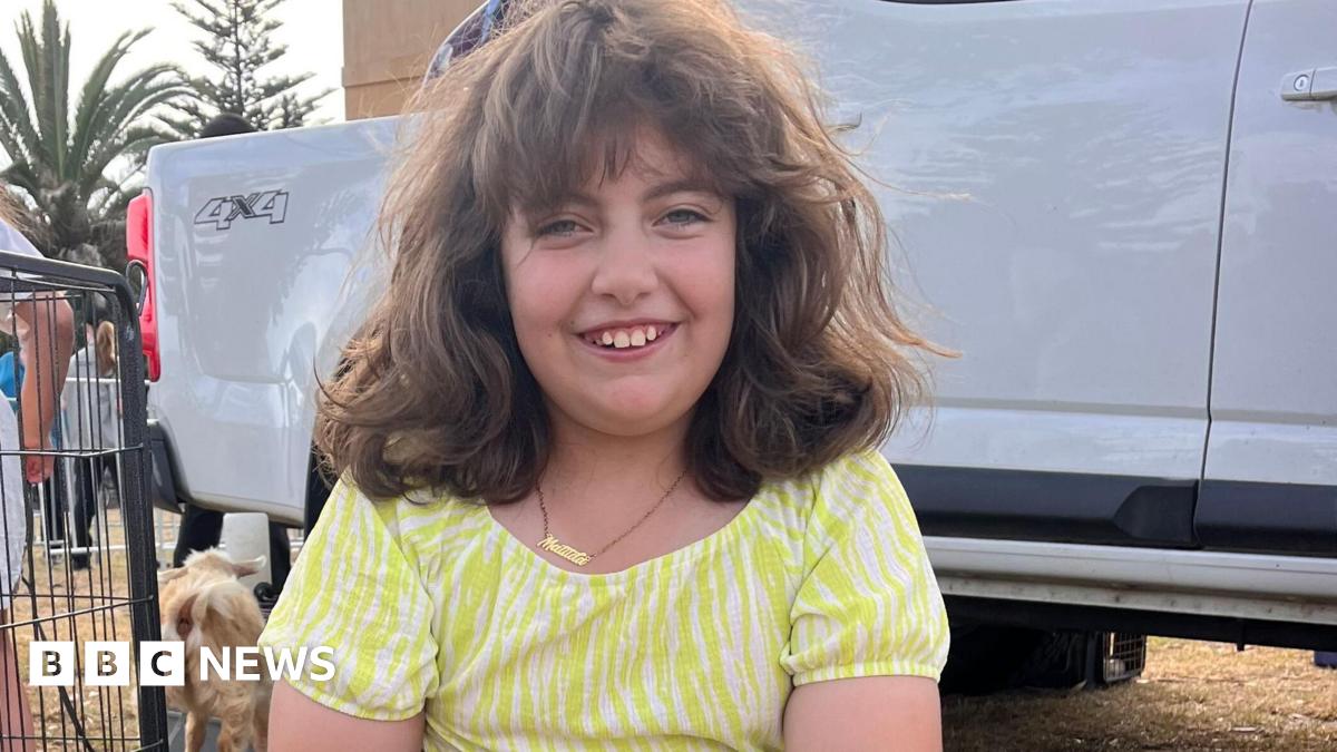 A young girl in a yellow striped dress smiles at the camera