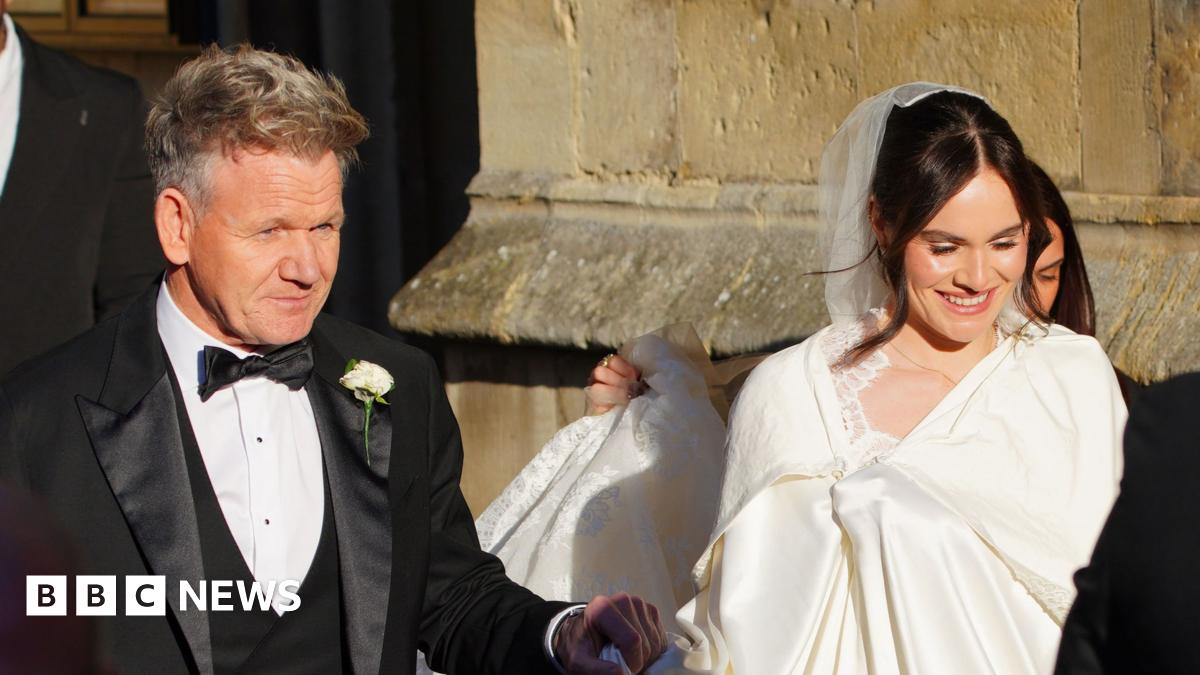 Gordon Ramsay pictured entering Bath Abbey with his daughter Holly. He is wearing a black suit and she is wearing a white dress and veil.