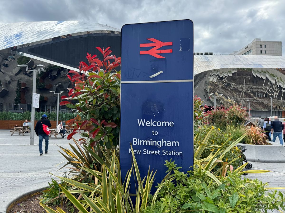 Birmingham New Street Station's Eastern Plaza with a Welcome to Birmingham New Street Station sign in navy blue with a red railway logo 