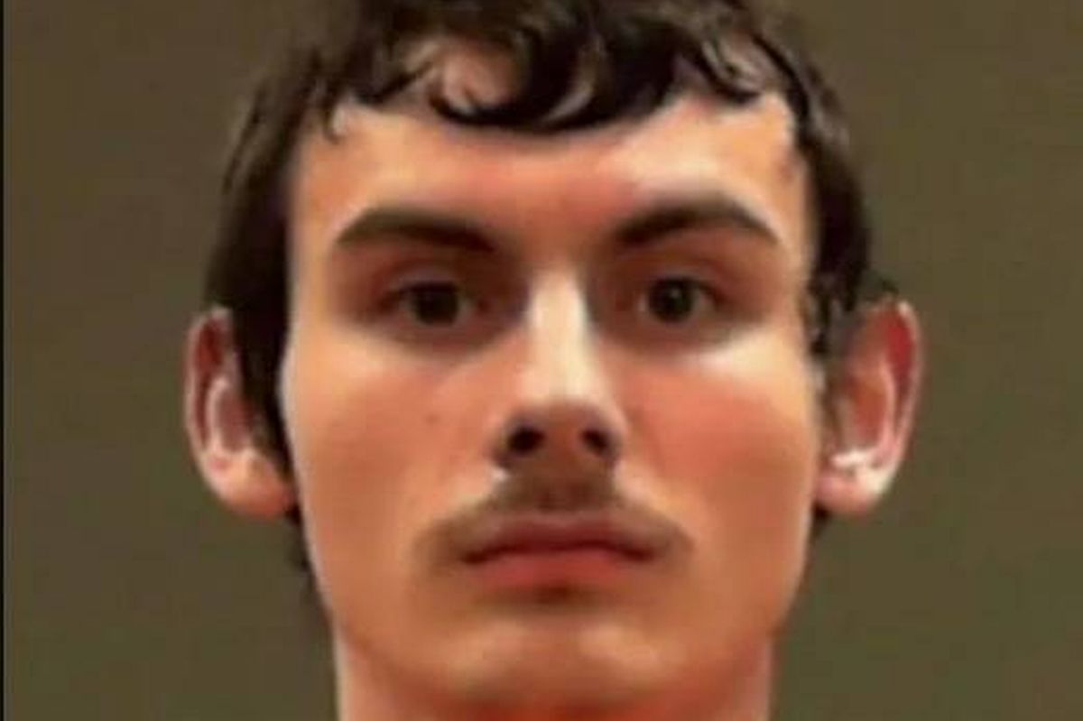 An individual with short, dark hair and a facial expression that conveys seriousness, featuring a prominent nose and a mustache, captured in a close-up against a plain background.