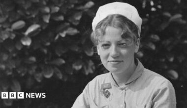 A black and white photo taken of Ann Remmers as a young midwife. She is wearing hospital scrubs and a white cap.  Her curly hair is pulled back and tucked underneath her cap, with a few pieces pulled out at the front.
